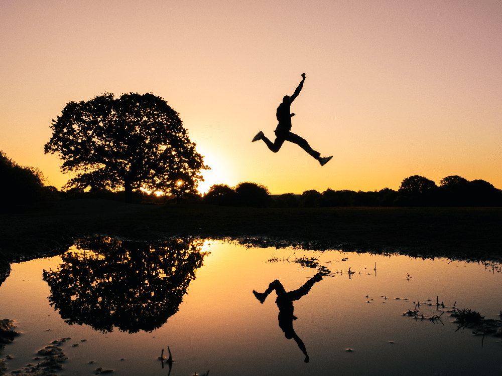 man jumping on body of water during golden hour